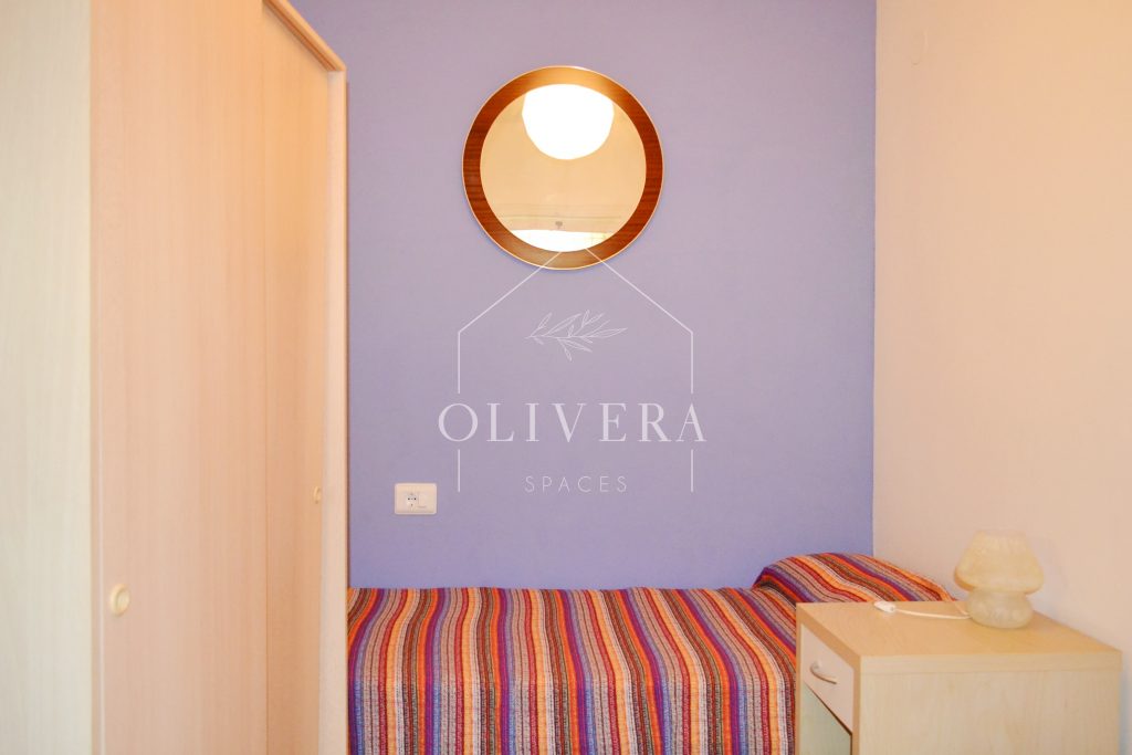 Habitación 3 con dos camas, mesitas, armario y espejo. Pared pintada de color lila.