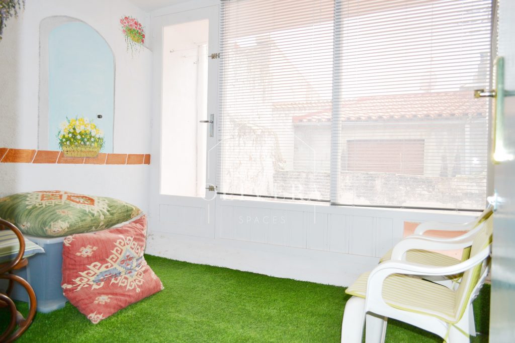 Galería o terraza interior muy luminosa, con césped artificial, butacas y mural pintado en la pared.