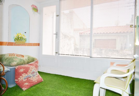 Galería o terraza interior muy luminosa, con césped artificial, butacas y mural pintado en la pared.