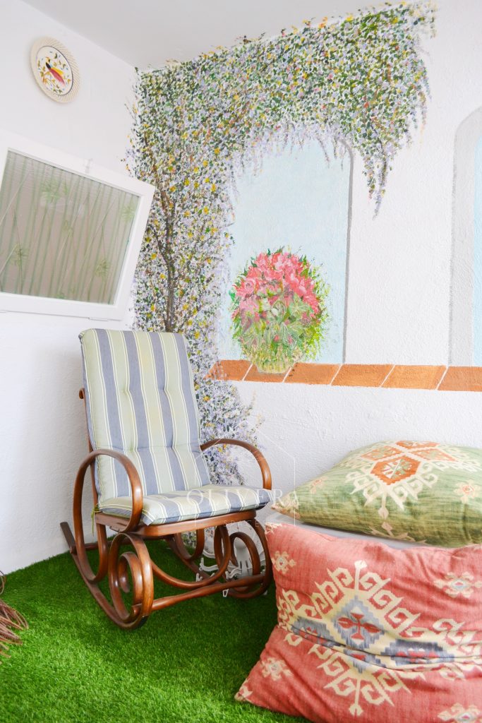 Galería o terraza interior muy luminosa, con césped artificial, butacas y mural pintado en la pared.