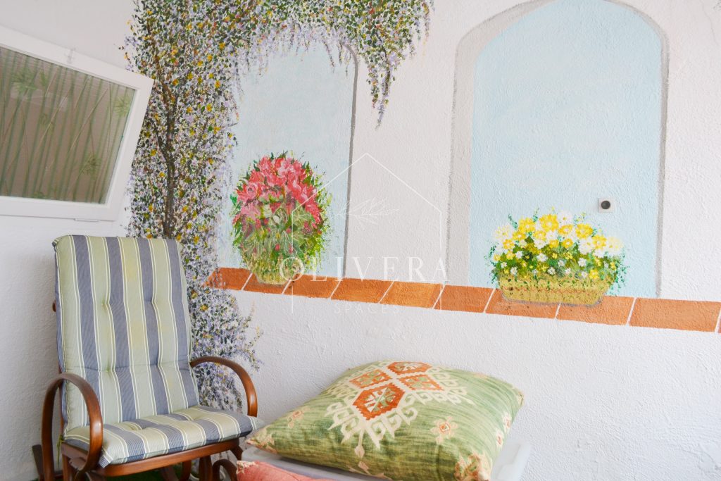 Galería o terraza interior muy luminosa, con césped artificial, butacas y mural pintado en la pared.
